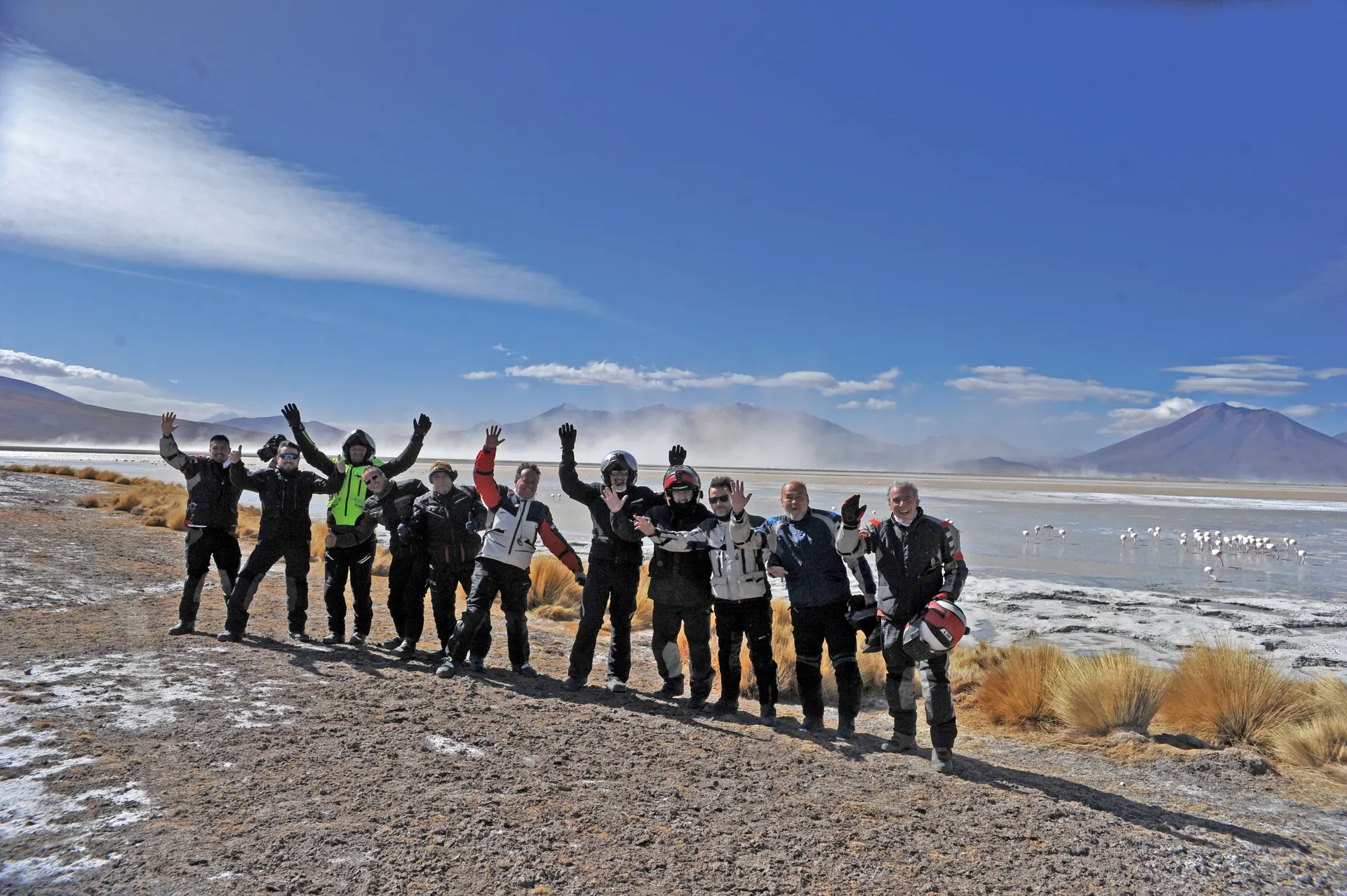 Grupo de viajeros de MotoTravel saludando junto a una laguna con flamencos en el altiplano boliviano