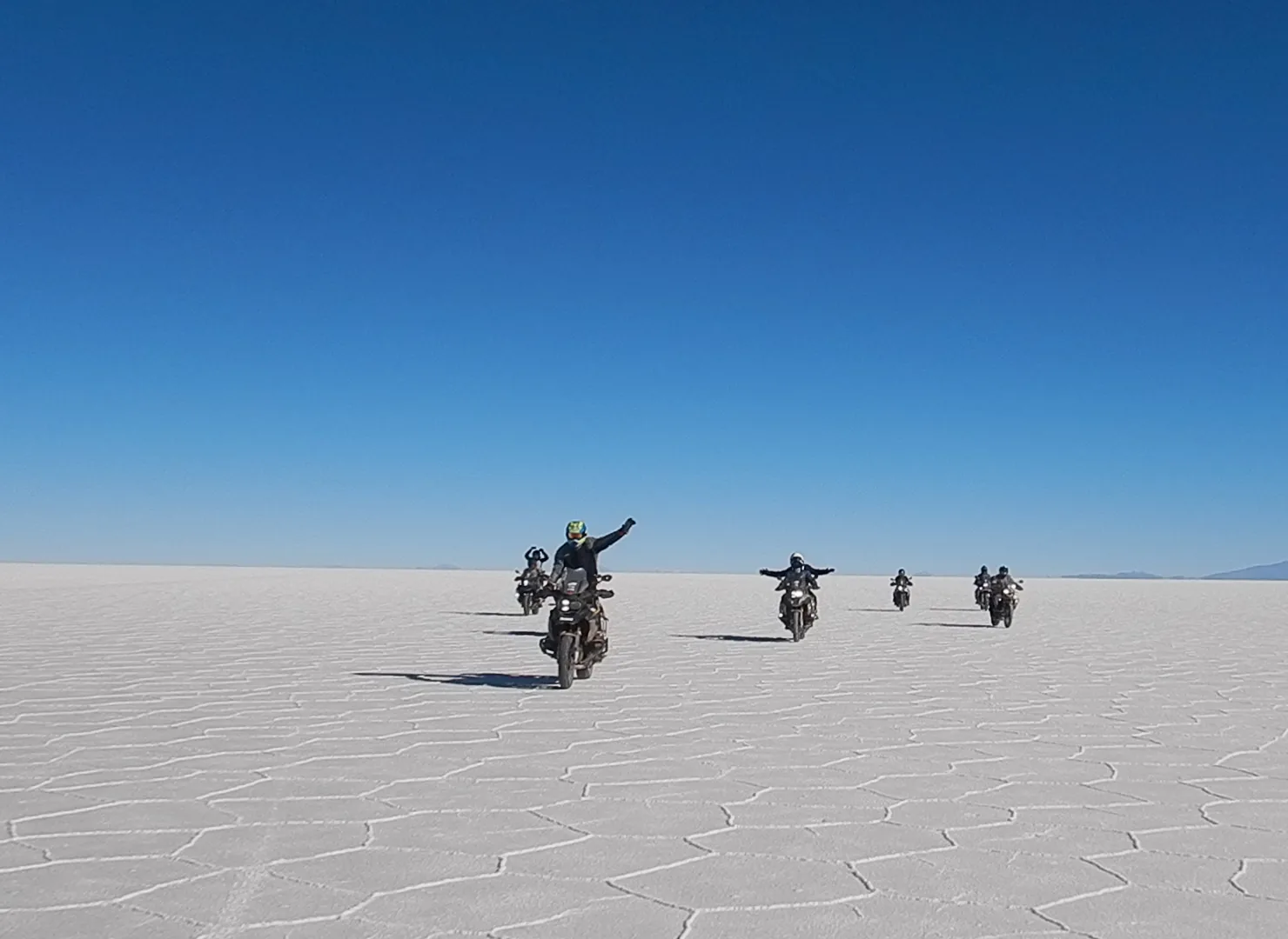 Grupo de motociclistas de MotoTravel saludando mientras cruzan el Salar de Uyuni, Bolivia